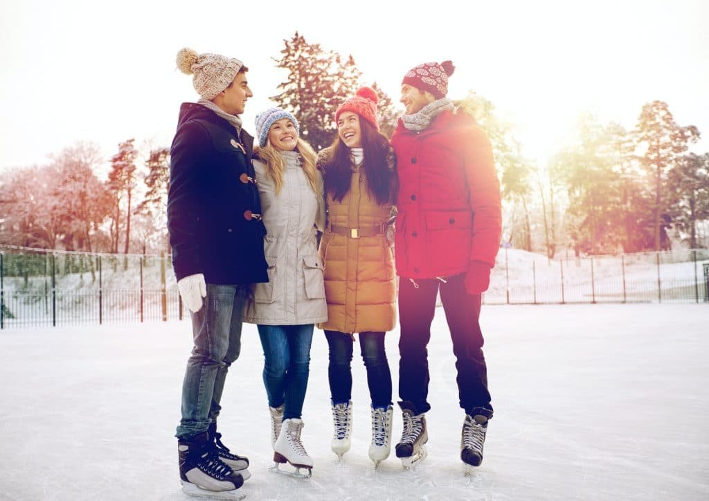 happy friends ice skating on rink outdoors