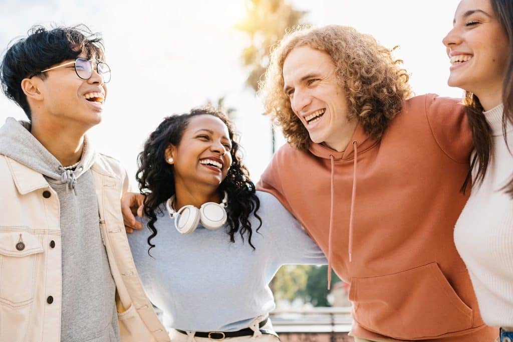 Group of happy young diverse teenage friends laughing together outdoors