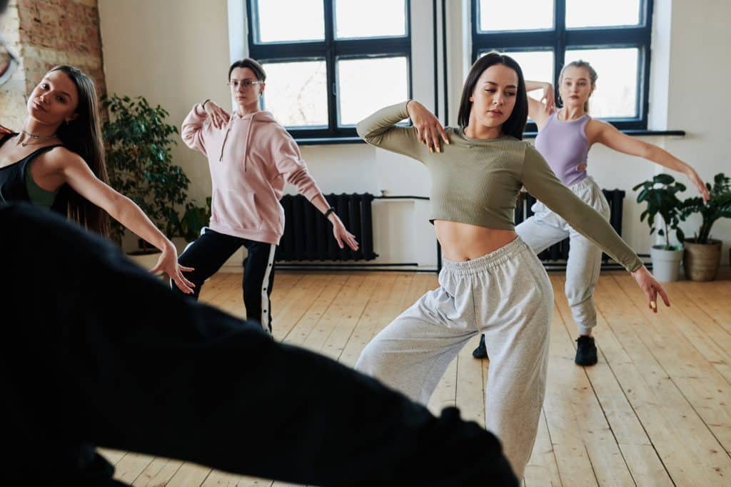 Teenage girls and guy repeating dancing exercise after instructor or leader
